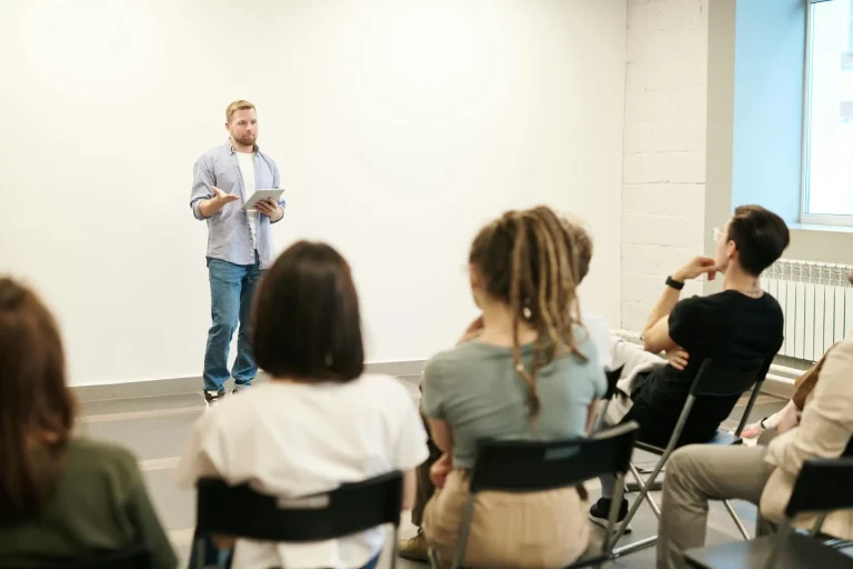 En la foto se ve a un persona dando una clase y delante suya los alumnos