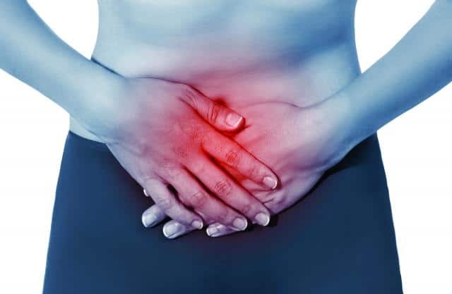 Dolor Pélvico, mujer con las manos en la zona del ombligo mostrando una zona de dolor en color rojo